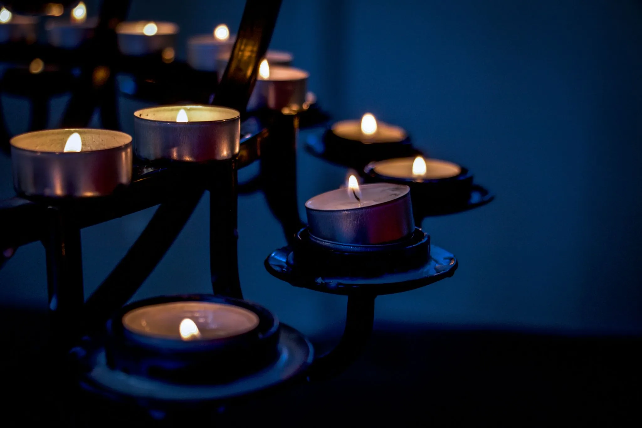 Lit votive candles on a dark metal stand.