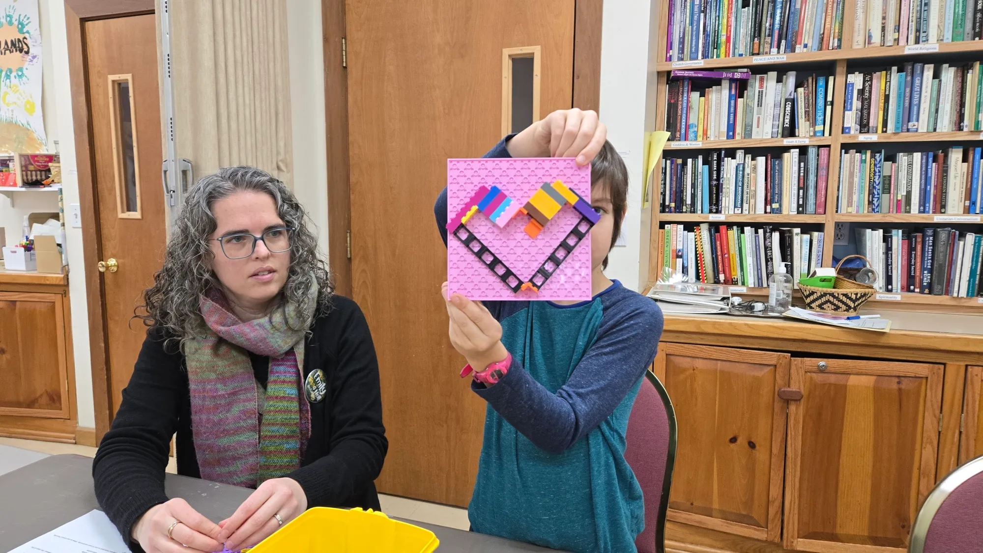 A child holds up a rainbow heart they built from LEGO bricks during a religious-education class
